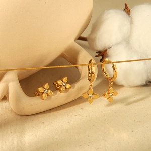 Golden clover earrings set with clear zircon stones on a decorative ceramic cup