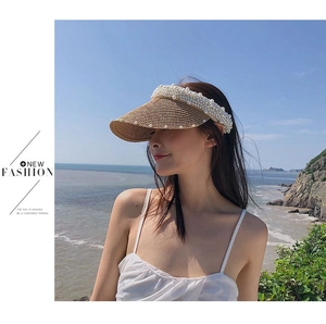 Detail of handmade straw visor with white pearl embellishments worn on a sunny beach