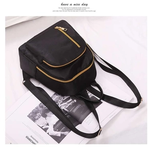 Detail view of black nylon backpack with golden zippers on a white textured background