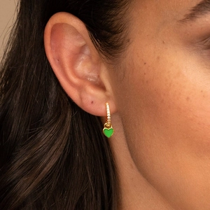Detailed close-up of green heart pendant hoop earrings with zircon pavé on a model
