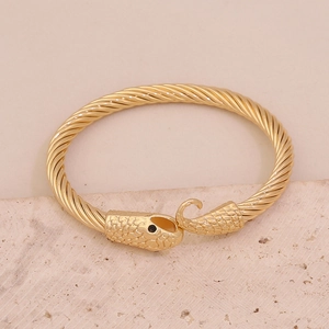 Dettaglio di un bracciale a serpente dorato testurizzato su pietra beige