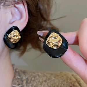 Macro shot of vintage black acetate earrings with hammered gold center on ear and hand