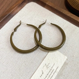 Detailed view of olive green geometric hoop earrings on textured white fabric display