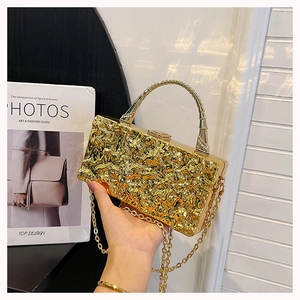 Detailed shot of golden acrylic box bag featuring unique metal texture and curved handle