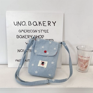 Detail van lichtblauwe denim telefoontas met witte sterren en rode knoop