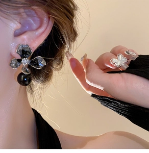 Detailed view of asymmetric black crystal flower earring with a hanging black pearl drop