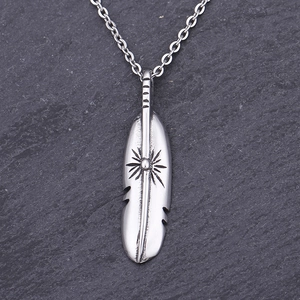 Detailed shot of a silver feather pendant necklace with sunflower engraving on dark rock