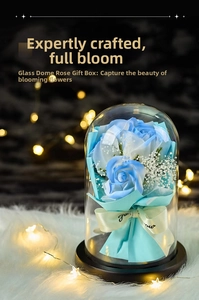 Close-up of blue preserved roses in a glass dome with warm bokeh lights and silk ribbon