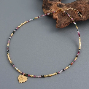 Colorful tourmaline beaded necklace with gold heart pendant and evil eye charm on grey base