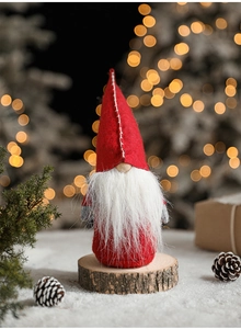 Detail of red knitted gnome decoration with long white beard on wooden base with bokeh light