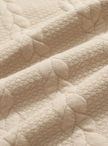 Macro view of beige floral jacquard knit fabric with soft quilted diamond texture detail
