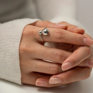 Close-up of silver double ball open ring on model hand with polished metal finish