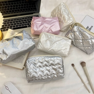 Flat lay of pink and silver heart-quilted cosmetic bags on a white bedding lifestyle scene
