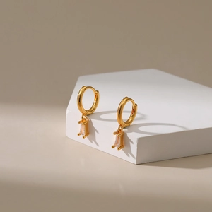 Macro shot of gold hoop earrings featuring rectangular zircon drops on a white stand