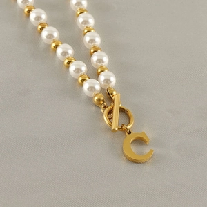 Detail of gold letter C pendant with elegant white pearls on a stainless steel chain