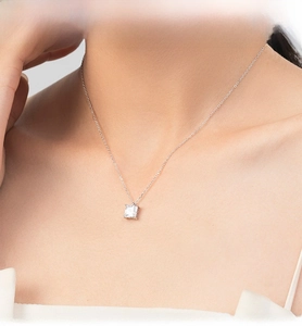 Detail of a square clear zircon pendant necklace worn on a woman's collarbone
