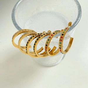 Detail of four pairs of gold C-shaped earrings with colorful stones on a glass rim