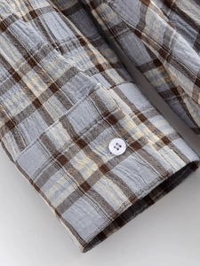 Detail eines karierten Hemdkleid-Ärmels mit weißem Harzknopf und Baumwoll-Leinen-Gewebe