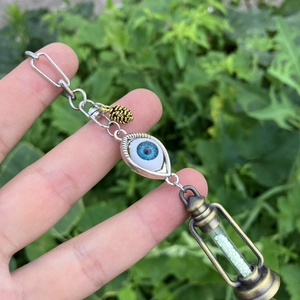 Close-up of vintage kerosene lamp pendant with blue eye and pine cone charms