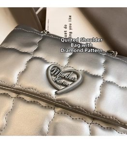 Close-up of quilted heart-shaped plaque and metallic chain on a silver backpack