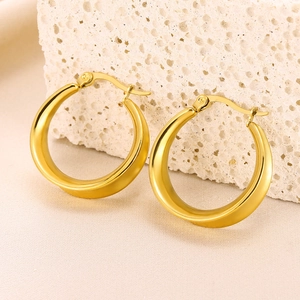 Detailed shot of golden geometric hollow hoop earrings on white textured stone surface