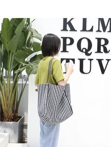 Side view of large black and white checkered canvas tote bag worn by a model in a minimalist room