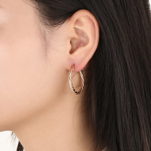 Detailed view of rose gold hoop earrings with a twisted rope texture on a model