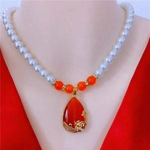 Detail of a pearl necklace featuring a red teardrop pendant and golden flower accents
