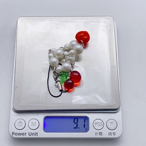 Détail d'une dragonne de téléphone cerise perlée y2k pesant 9,1g sur une balance