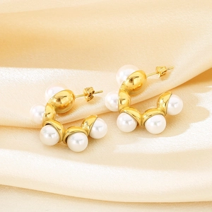 Detail shot of gold C-shaped earrings with white pearls on elegant silk background