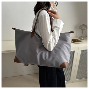 Detailed view of gray oxford fabric tote bag with brown leather handles worn by a model