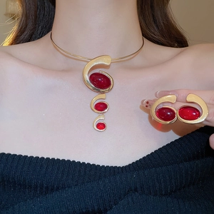 Close-up of gold metal choker necklace and earrings set with red oval resin stones