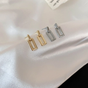 Close-up of gold and silver geometric rectangular earrings on white silk fabric