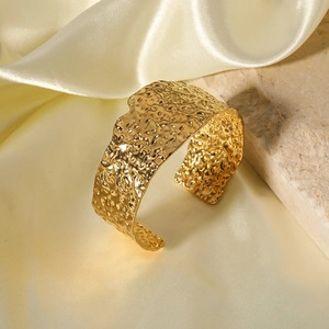 Macro detail of wide gold hammered texture cuff bracelet on elegant silk background