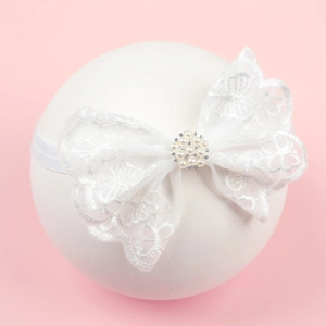 White baby lace bow headband with pearls and rhinestones on a pink background