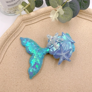 Detail of sequin mermaid tail, starfish and seashell hair clips on a beige tray