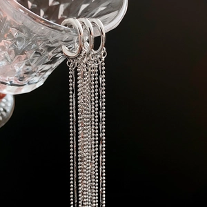 Silver tassel earrings with fine chain beads hanging on faceted glass with a dark background