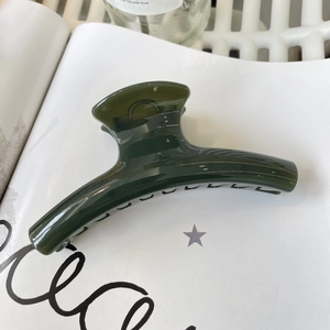 Macro shot of large dark green hair claw clip with glossy finish on a white art book