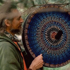 Handmade shamanic drum with blue mandala pattern played in a forest setting