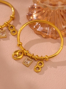 Macro shot of gold stainless steel bangle with rectangle crystal and figure eight charms