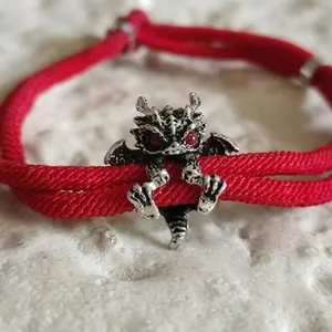 Détail macro d'un bracelet tressé rouge avec breloque dragon argenté et yeux rouges