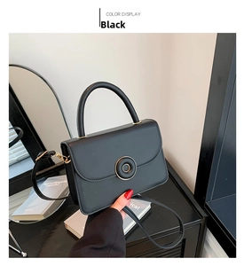 Detailed view of a black leather crossbody bag with a gold round buckle and top handle