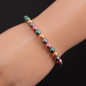 Dettaglio del bracciale con perle multicolore in toni verde, rosa e grigio al polso