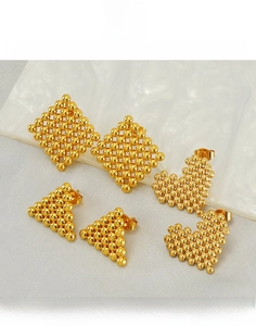 Détail de boucles d'oreilles géométriques en acier titane doré sur fond de marbre