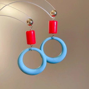 Detail of color-block geometric earrings featuring red beads and blue resin rings