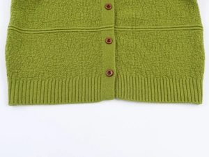 Close-up of green bouclé knit cardigan featuring brown buttons and ribbed hem detail