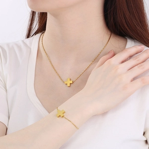 Detail of gold cross pendant necklace and adjustable bracelet set worn on a model