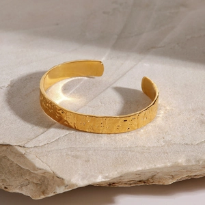Brazalete dorado con textura martillada y diseño ondulado sobre base de piedra