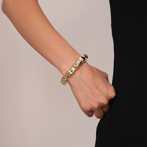 Detailed close-up of golden wide cuff with irregular lava texture on model wrist