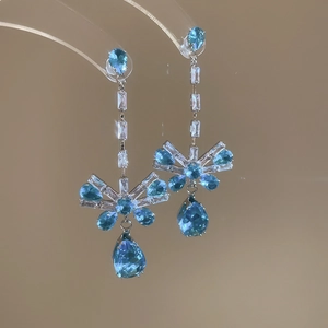 Detail of silver bow earrings with blue teardrop crystals on a display stand